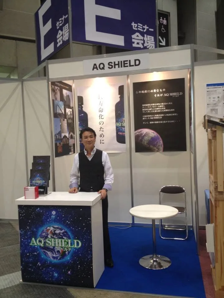 2013年の東京ビッグサイトでの AQ SHIELD リキッドクリスタル発売時展示会ブースに立つ二宮不二雄